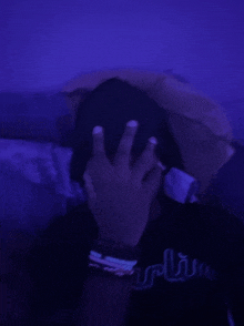 a person is covering their face with their hand in a dark room with purple lights .