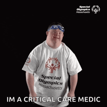 a man with down syndrome wearing a special olympics t-shirt and goggles is standing in front of a black background .