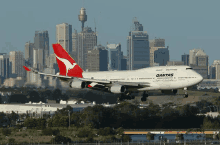 a qantas plane is taking off from a runway in front of a city skyline