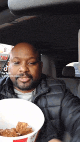 a man sitting in a car holding a bucket of food