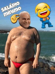 a man in red swim trunks stands on a rocky beach next to the ocean and a smiley face that says salario minimum