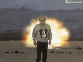 a man wearing a sweater with a dog on it is standing in front of an explosion sponsored by quickbooks