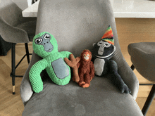 three stuffed animals are on a chair including a green monkey