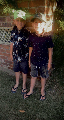 two young boys standing next to each other wearing flip flops and hats