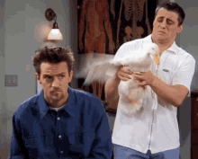 a man in a blue shirt holds a duck while another man holds a white duck