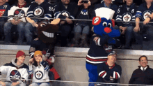 a group of people sitting in a stadium watching a hockey game with a mascot wearing a chef 's hat