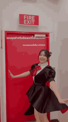 a girl in a black dress is standing in front of a red door that says fire exit