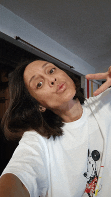 a woman wearing a white t-shirt with mickey mouse on it makes a peace sign