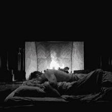 a couple is laying in bed in front of a fireplace .