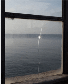 a broken window with a view of the ocean and the sun shining through it