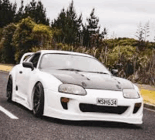 a white sports car is parked on the side of a road .