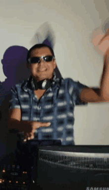 a man wearing sunglasses and headphones is dancing in front of a samsung monitor