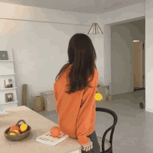 a woman in an orange sweater is standing in front of a table with a book on it that says " poetry "