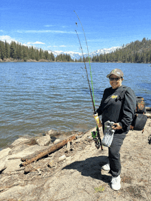 a woman holding a fishing rod in front of a lake with mountains in the distance