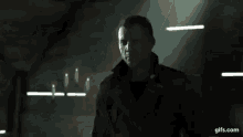 a man in a black coat is standing in a dark room with a light shining on him .