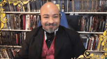 a man in a tuxedo is sitting in front of a bookshelf with a book titled " the hobbit " on the top