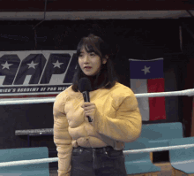 a woman stands in a boxing ring holding a microphone in front of a sign that says ' sap '