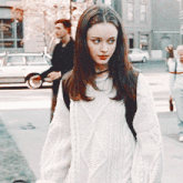 a woman wearing a white sweater is walking down a sidewalk