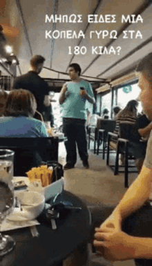 a man in a blue shirt stands in front of a group of people in a restaurant with a sign above him that says 180 kilo