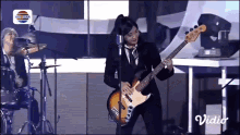 a woman in a suit is playing a guitar in front of a drum set