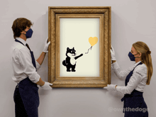 two people holding up a framed picture of a dog holding a yellow balloon