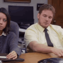 a man and a woman are sitting at a table with a phone in front of them