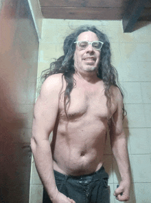 a shirtless man with long hair and glasses stands in a bathroom