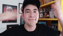 a young man wearing a hat and a black shirt is standing in front of a bookshelf with toys on it ..