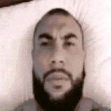 a man with a beard is laying on a bed with a white pillow .