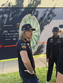 a man wearing a red bull shirt stands in front of a dartboard