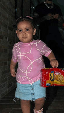 a little girl in a pink shirt holding a bag of ritz crackers