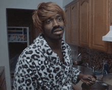 a man wearing a leopard print robe and wig is standing in a kitchen