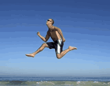 a shirtless man is jumping in the air on the beach