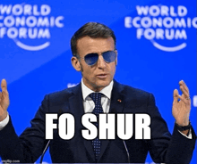 a man in a suit and tie stands in front of a world economic forum sign