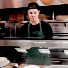 a man in a green apron stands in front of a display of pizza boxes that say ' fancy ' on them