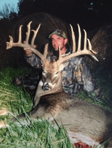 a man in a camo jacket holds up a large deer