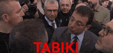 a man in a suit and tie is surrounded by other men and the word tabiki is written in red