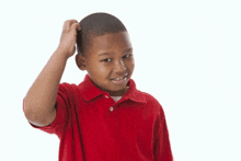 a young boy in a red shirt scratching his head