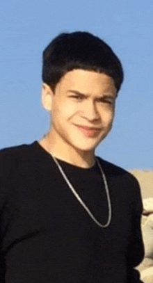 a young man wearing a black shirt and a silver chain is smiling .