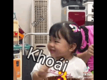 a little girl is making a funny face in front of a fan and a refrigerator .