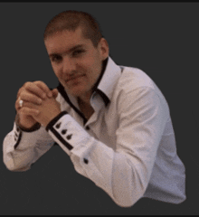 a man in a white shirt with black cuffs is sitting with his hands folded