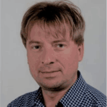 a man is wearing a blue and white checkered shirt and smiling for the camera .