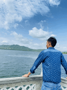 a man in a blue shirt is looking out over a lake