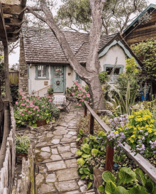 a stone walkway leads to a small house with flowers in front of it