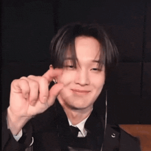 a man in a suit and tie is smiling and making a heart shape with his hands .