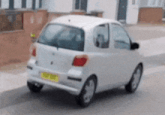 a small white car is parked on the side of the road with a yellow plate