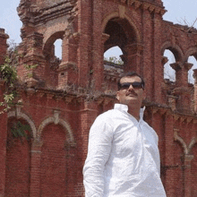 a man wearing sunglasses is standing in front of a red brick building .