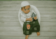 a little boy wearing a white hat and green pants is sitting on a chair holding a book