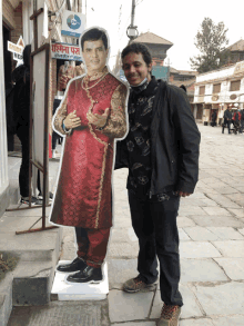 a man stands in front of a cardboard cutout of a man in a red dress