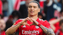 a soccer player in a red emirates jersey is making a heart shape with his hands .